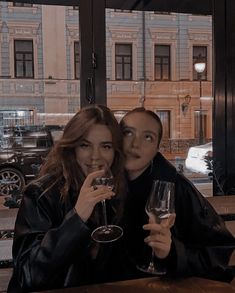 two people sitting at a table with wine glasses in front of them and looking into the camera