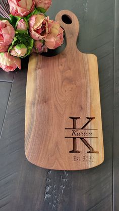 a wooden cutting board with a monogrammed initial on it and flowers next to it