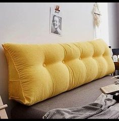 a bed with a yellow pillow on top of it next to a book and some pictures