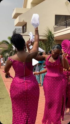 two women in bright pink dresses are dancing with their hands up and one woman is holding a white object