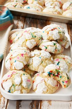 cookies with sprinkles are on a white plate next to a tray of cookies