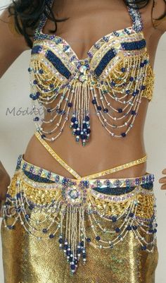 a woman in a gold and blue belly dance outfit with beads on her chest,