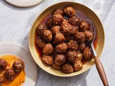 meatballs and sauce in a bowl on a marble counter top with a wooden spoon