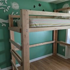 a wooden bunk bed sitting next to a window in a room with green walls and hardwood floors