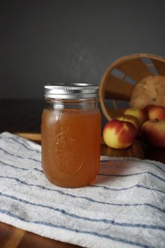 a glass jar filled with liquid sitting on top of a table next to apples and a basket