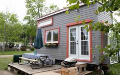 a small gray house with red trim on the windows and doors is sitting in front of a picnic table