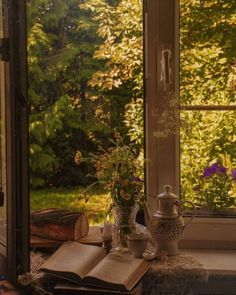 an open book sitting on top of a window sill next to a vase filled with flowers