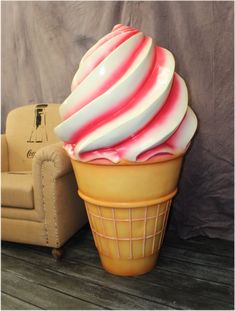 a large ice cream cone sitting on top of a wooden floor next to a chair