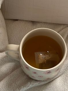 a cup of tea sitting on top of a bed next to a pillow and blanket