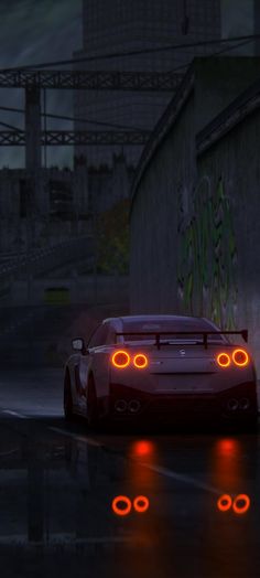 a red sports car driving down a wet road at night with its headlights turned on