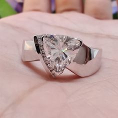 a woman's hand holding a ring with a heart shaped diamond in the center