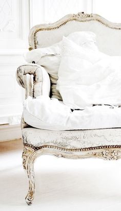 an old chair with white sheets and pillows on it