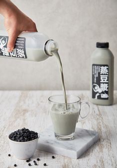 a person pouring milk into a cup with blackberries on the table next to it