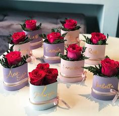 six small pink and purple boxes with red roses in them on a white tablecloth