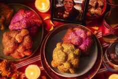 a table topped with plates and bowls filled with food next to candlelight candles on top of a red cloth covered table