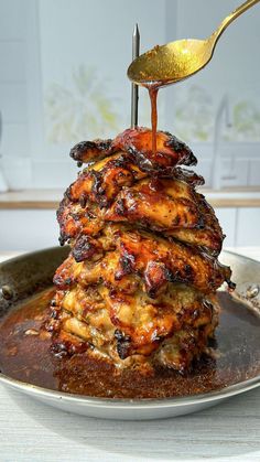 a stack of pancakes with syrup being poured onto them on a silver plate and gold spoon