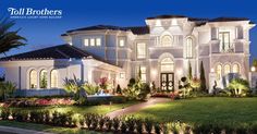 a large white house lit up at night with palm trees and bushes in front of it