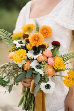 a woman holding a bouquet of flowers in her hands and wearing a white dress with an orange sash around her waist