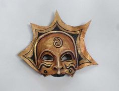 a mask is hanging on the wall in front of a white background with an orange and black design