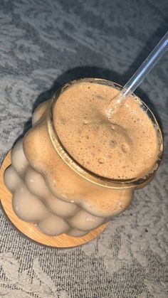 a glass filled with liquid sitting on top of a wooden bowl next to a metal straw