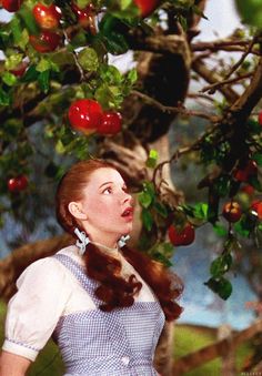 a woman standing under a tree with apples on it