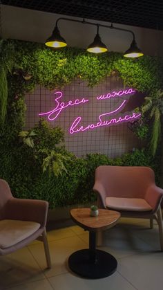 two chairs and a table in front of a green wall with neon signs on it