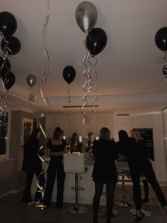 some people are standing in a room with black and silver balloons