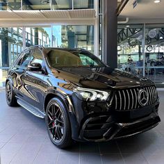 a black mercedes suv is parked in front of a glass building with lots of windows