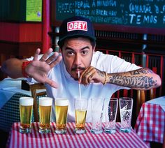 a man sitting at a table with lots of glasses in front of him and drinking from a straw