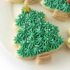 decorated cookies on a white plate with green icing and gold stars in the shape of a christmas tree