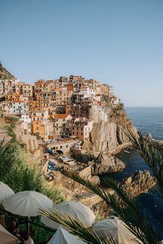 people are sitting under umbrellas near the water and buildings on top of a hill