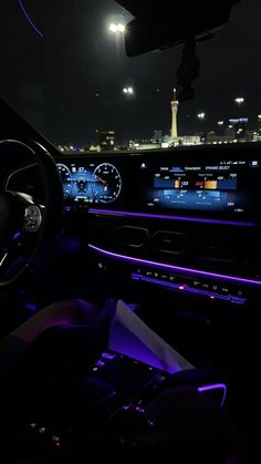 the interior of a car with illuminated dashboard lights and electronic controls at night, in front of a cityscape