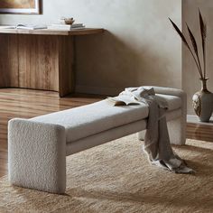 a white bench sitting on top of a wooden floor next to a vase with flowers