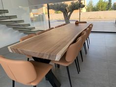 a wooden table surrounded by brown chairs in front of a glass wall with stairs leading up to the second floor