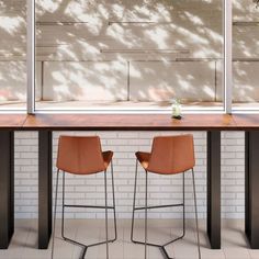 two chairs sitting on top of a wooden table next to a white brick wall and tree