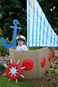 a little boy sitting in a cardboard boat made to look like a sailboat and an anchor