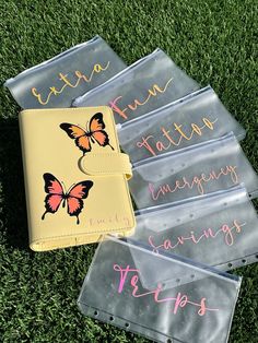 four butterflies on clear plastic bags with pink and yellow writing in the middle, sitting on green grass