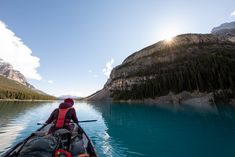 a person in a kayak paddling on the water with mountains in the background