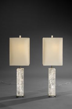 a pair of marble lamps with white shades on each lamp and one light turned off