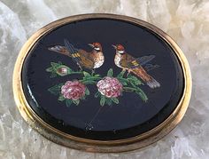 a small black box with two birds and flowers painted on the inside, sitting on top of marble