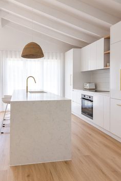 a white kitchen with an island in the middle and wood flooring on the other side