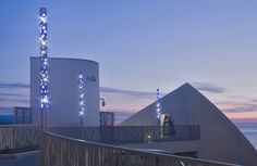 a white building with blue lights on it's side next to the ocean at dusk