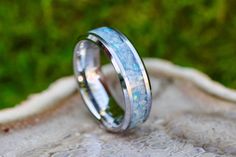 two wedding rings sitting on top of a white marbled surface with green grass in the background