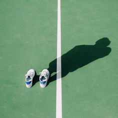 two tennis shoes sitting on top of a tennis court next to a white line with the shadow of a person's foot