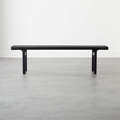 a black bench sitting on top of a cement floor next to a white wall in an empty room