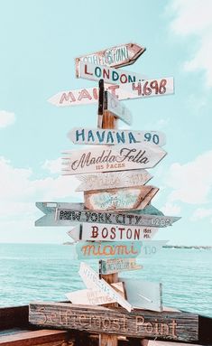 a bunch of signs that are on top of a wooden pole near the ocean and some water