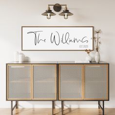 a white sign that says the williamss above a sideboard with two vases on it