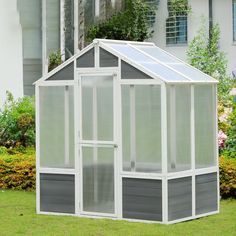 a small white greenhouse in the middle of some grass