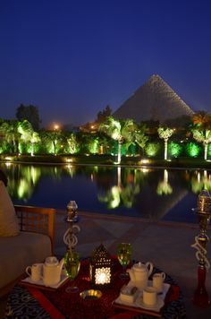 a table with tea cups and plates on it in front of a pool at night