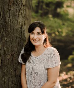 a woman standing next to a tree in the woods